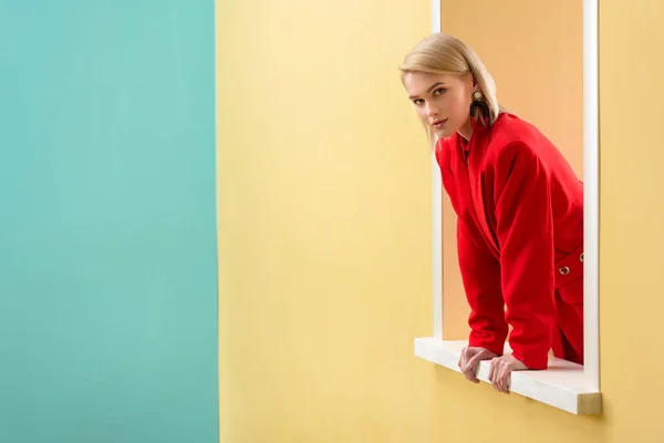 Молода стильна жінка в червоному костюмі дивиться декоративне вікно — стокове фото
