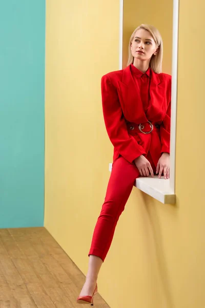 Beautiful pensive woman in stylish red suit sitting on decorative window — Stock Photo