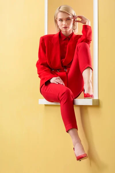 Hermosa mujer rubia en elegante traje rojo y zapatos sentados en la ventana decorativa — Stock Photo