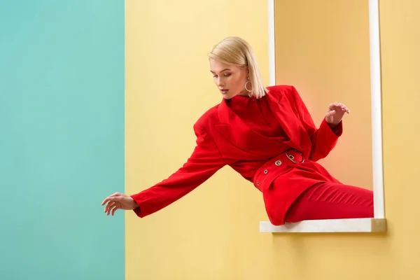 Jeune femme à la mode en costume rouge regardant par la fenêtre décorative — Photo de stock