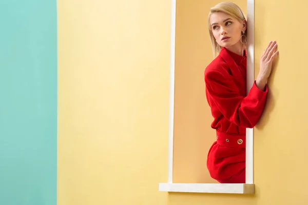 Chère femme à la mode en costume rouge regardant par la fenêtre décorative — Photo de stock