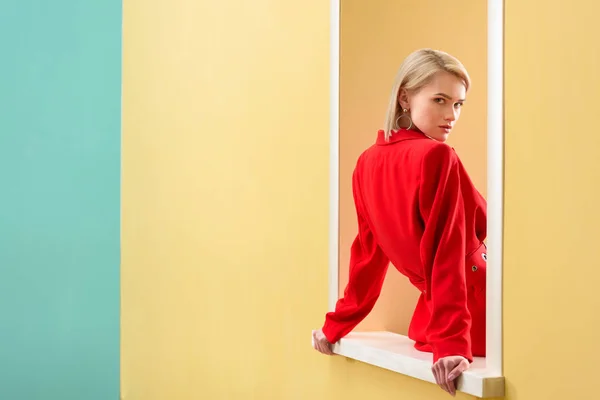 Jovem mulher na moda em terno vermelho olhando para fora janela decorativa — Fotografia de Stock