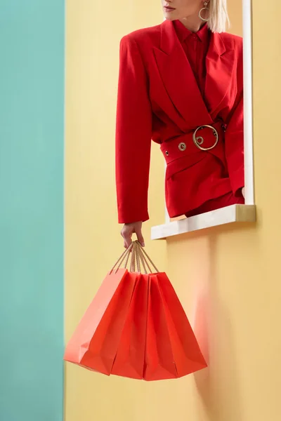 Schnappschuss einer modischen Frau in roter Kleidung mit roten Einkaufstüten, die auf einem dekorativen Fenster sitzt — Stockfoto