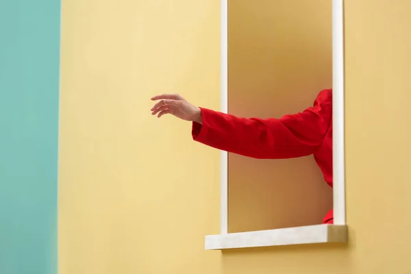 Tiro cortado de mulher em casaco vermelho colando mão para fora janela decorativa — Fotografia de Stock