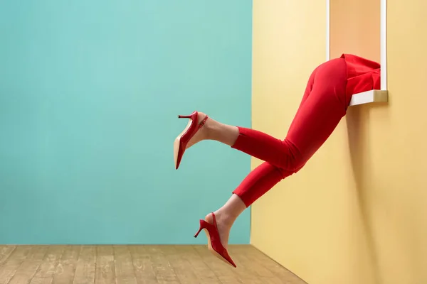 Vista parcial de la mujer en pantalones rojos y zapatos colgando de la ventana decorativa - foto de stock