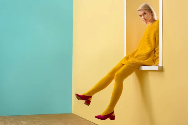 Side view of stylish woman in pink shoes, yellow sweater and tights sitting on decorative window — Stock Photo