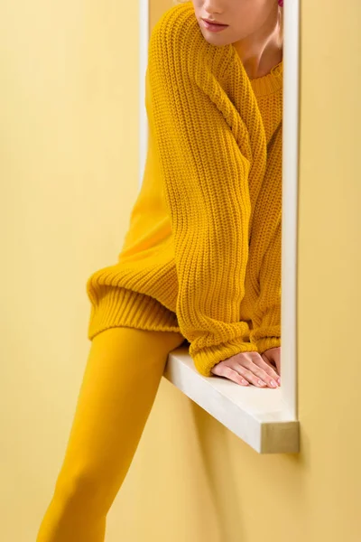 Cropped shot of stylish woman in yellow sweater and tights sitting on decorative window — Stock Photo