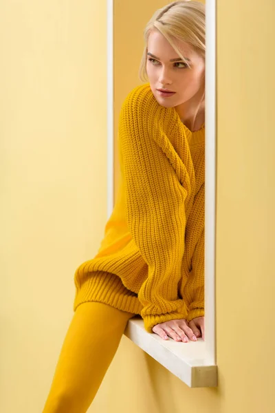 Partial view of stylish pensive woman in yellow sweater and tights sitting on decorative window — Stock Photo