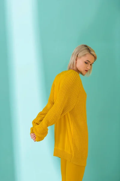Vista lateral de la hermosa mujer en suéter amarillo y medias posando sobre fondo azul - foto de stock