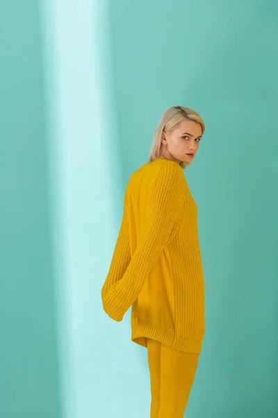 Vista laterale della giovane donna in maglione giallo e collant in posa su sfondo blu — Foto stock