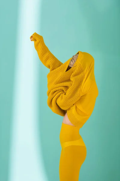 Vista lateral de la mujer en medias amarillas con suéter amarillo posando sobre fondo azul - foto de stock