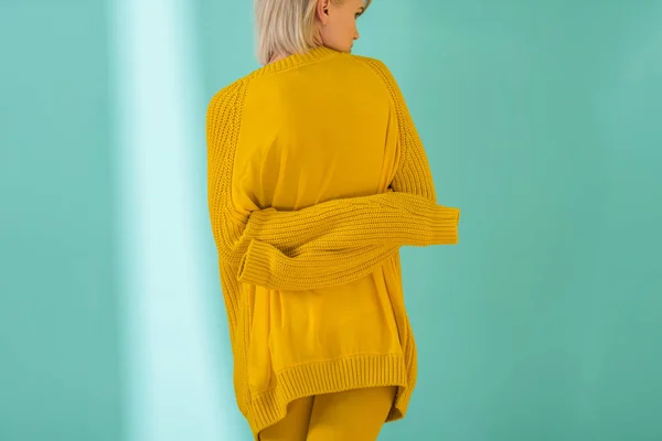 Vue arrière de la femme en pull jaune posant sur fond bleu — Photo de stock