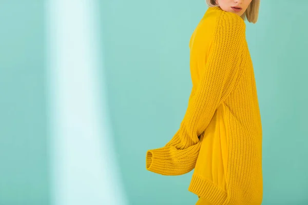 Vista parcial de la mujer en suéter amarillo posando sobre fondo azul - foto de stock