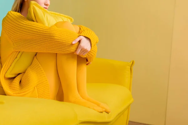 Partial view of woman in yellow sweater and tights sitting on yellow sofa — Stock Photo