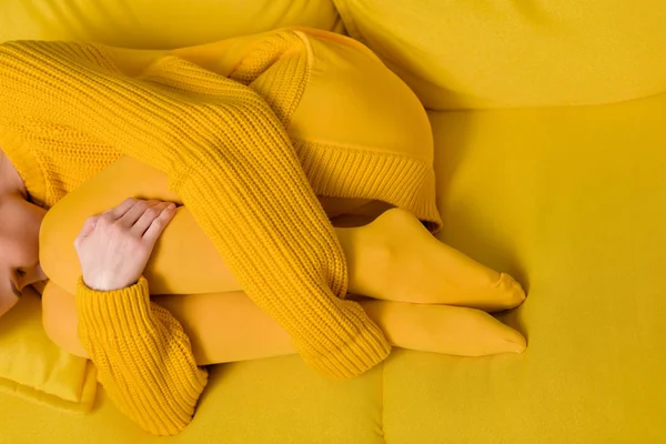 Vista parcial de la mujer en suéter amarillo y medias durmiendo en sofá amarillo - foto de stock