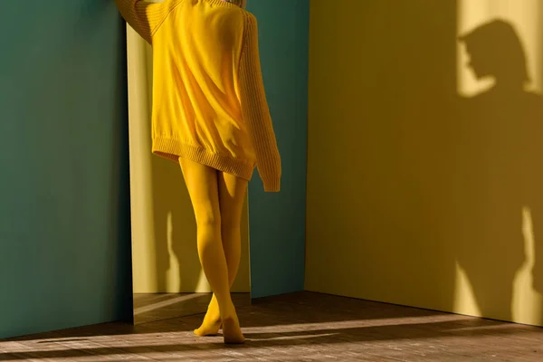 Colpo ritagliato di donna in maglione giallo e collant in piedi a specchio — Foto stock