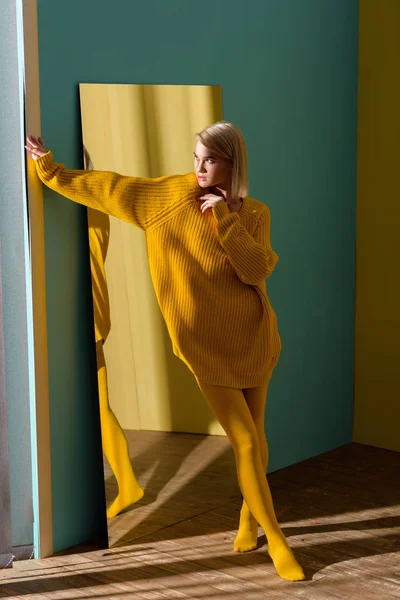 Mujer rubia con estilo en suéter amarillo y medias de pie en el espejo - foto de stock