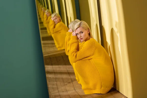 Side view of beautiful thoughtful woman in yellow sweater sitting at mirror with her reflection in it — Stock Photo