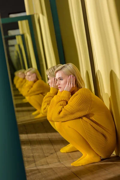 Vista lateral da bela mulher pensativa em suéter amarelo sentado no espelho com seu reflexo nele — Fotografia de Stock
