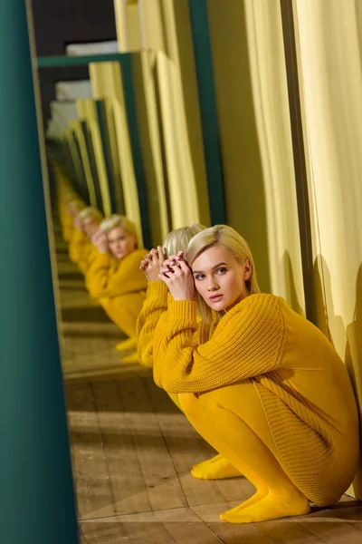 Vue latérale de belle jeune femme en pull jaune assis au miroir avec son reflet dedans — Photo de stock