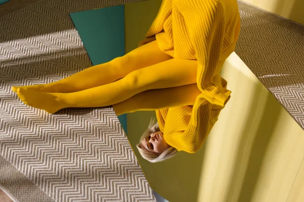 Partial view of woman in yellow sweater and tights sitting on mirror with reflection in it — Stock Photo