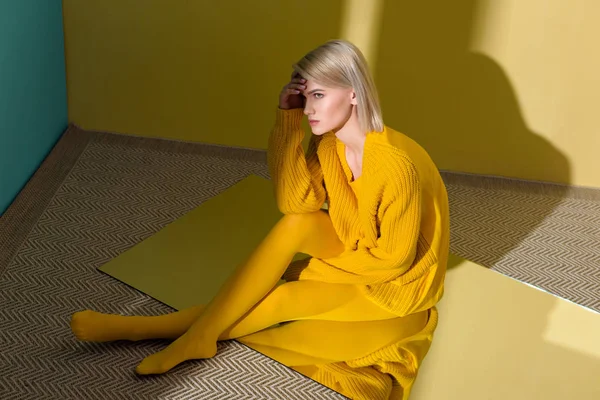 Высокий угол обзора красивой молодой женщины в желтом свитере и колготках, сидящих на зеркале с отражением в нем — стоковое фото