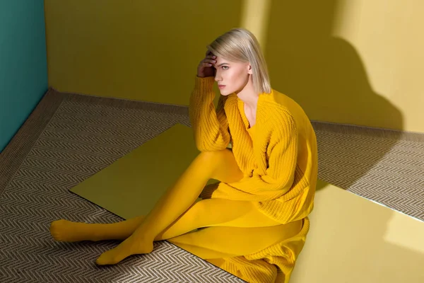 High angle view of beautiful young woman in yellow sweater and tights sitting on mirror with reflection in it — Stock Photo