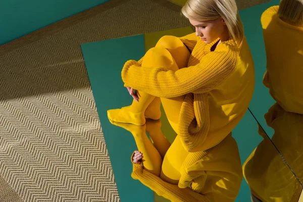 Side view of woman in yellow sweater and tights sitting on mirror with reflection in it — Stock Photo