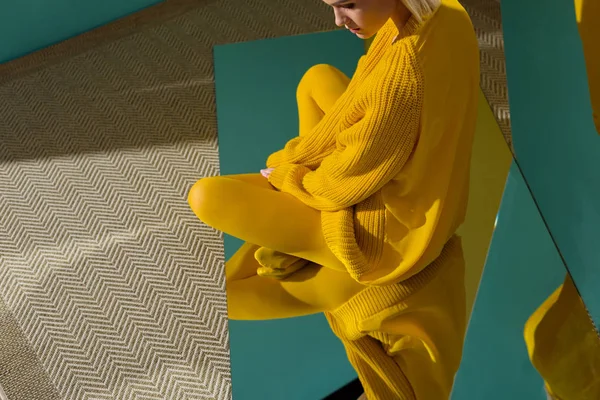 Cropped shot of woman in yellow sweater and tights sitting on mirror with reflection in it — Stock Photo