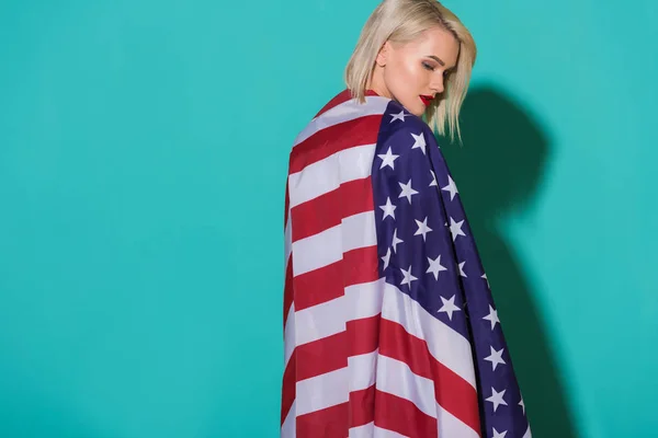 Vista trasera de mujer joven con bandera americana sobre fondo azul, celebrando el concepto del 4 de julio - foto de stock