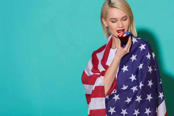 Porträt einer jungen Frau mit amerikanischer Flagge und Cupcake auf blauem Hintergrund, die den 4. Juli feiert — Stockfoto