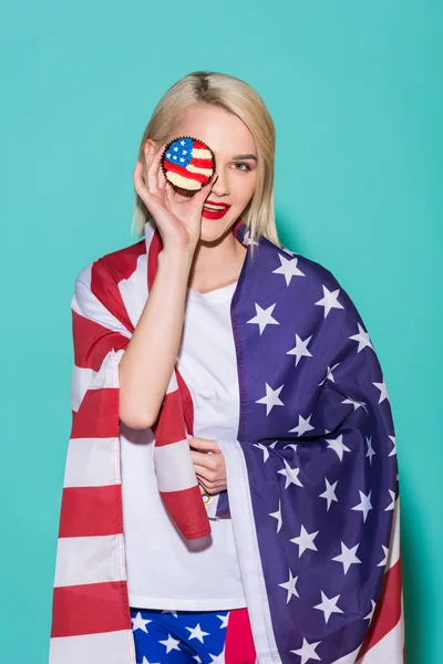 Portrait of young woman with american flag and cupcake on blue backdrop, celebrating 4th july concept — Stock Photo