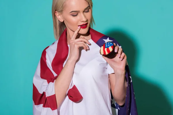 Portrait of attractive woman with american flag and cupcake on blue backdrop, celebrating 4th july concept — Stock Photo