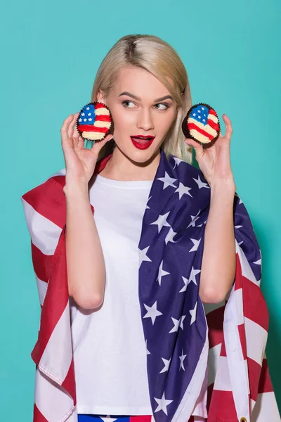 Retrato de uma jovem com bandeira americana e cupcakes em fundo azul, celebrando o conceito de 4 de julho — Fotografia de Stock