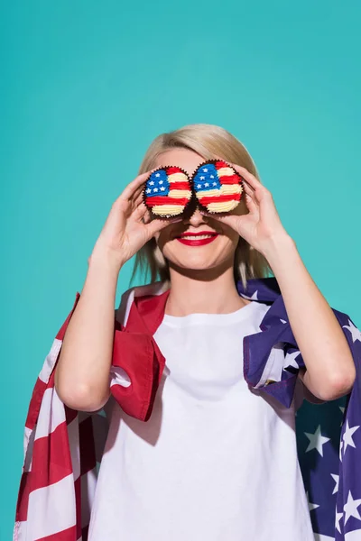 Vista oscurecida de una mujer sonriente con bandera americana y cupcakes sobre fondo azul, celebrando el concepto del 4 de julio - foto de stock