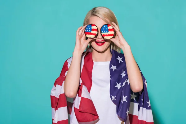 Vista oscurecida de la mujer alegre con bandera americana y cupcakes en el telón de fondo azul, celebrando el concepto del 4 de julio - foto de stock