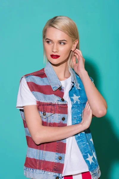 Portrait of stylish young woman in denim jacket with american flag pattern posing on blue backdrop — Stock Photo