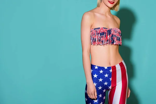 Plan recadré de femme souriante en haut et leggings avec motif drapeau américain posant sur fond bleu — Photo de stock