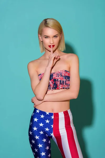 Ritratto di bella donna in alto e leggings con motivo bandiera americana che mostra segno di silenzio su sfondo blu — Foto stock