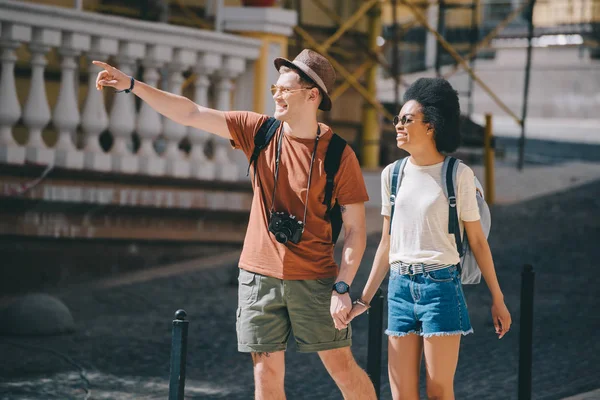 Homem viajante com câmera apontando por dedo para Africano americano namorada andando perto — Fotografia de Stock
