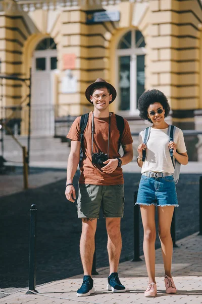 Casal de jovens turistas com câmera e mochilas em pé na rua — Fotografia de Stock