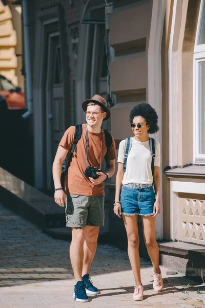 Interracial couple of young tourists with camera walking on street — Stock Photo