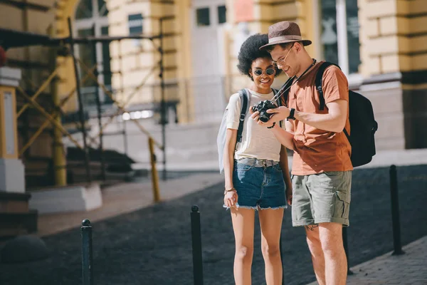 Sonriente pareja de jóvenes turistas que buscan fotografías en la pantalla de la cámara - foto de stock