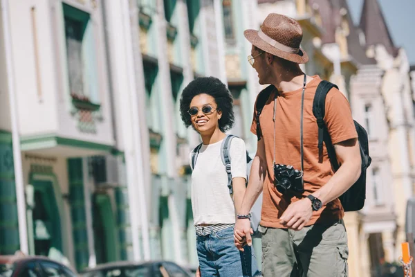 Male traveler with camera holding hand of african american girlfriend — Stock Photo