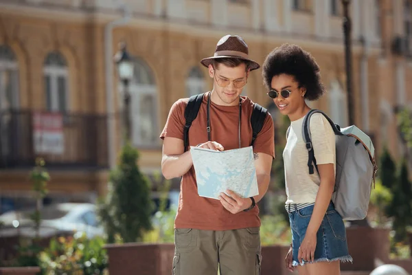 Young male traveler pointing at map to african american girlfriend standing near — Stock Photo