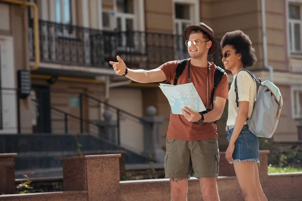 Young male traveler with map pointing to african american girlfriend — Stock Photo