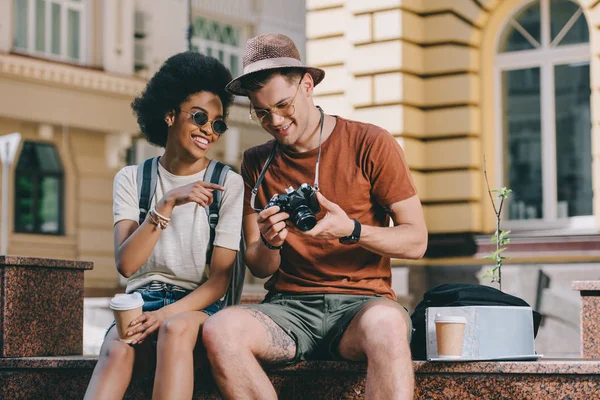 Smiling african american female traveler pointing on camera screen to boyfriend — Stock Photo