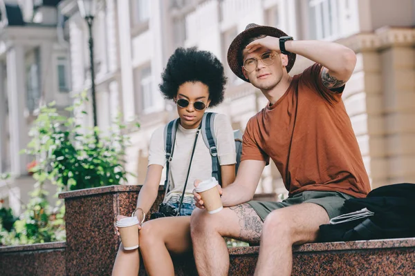 Multicultural couple of young tourists sitting with coffee cups — Stock Photo