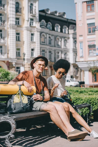 Young multicultural couple of tourists with bottles of water resting on bench — Stock Photo