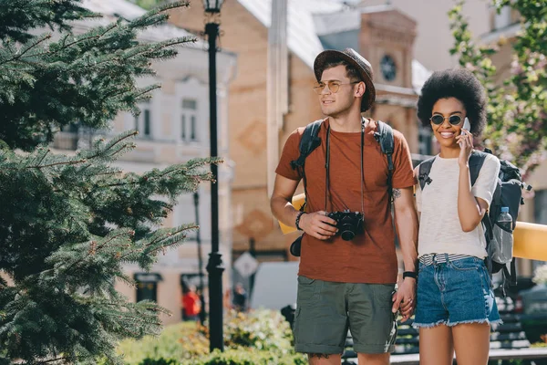 Africano americano mujer turista hablando en smartphone y su novio con cámara - foto de stock